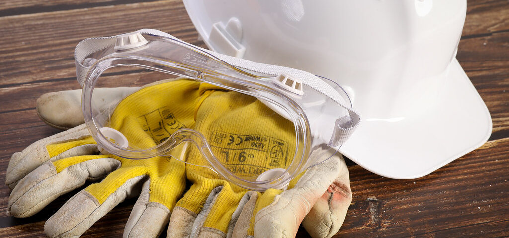 Safety gloves with protective helmet and glasses on wooden background